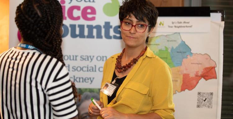 Two women talking in front of a Healthwatch banner